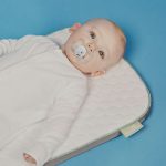 baby in white onesie lying on bed